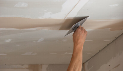 A man puts putty on a plasterboard ceiling. Putty for the joints of plasterboard sheets