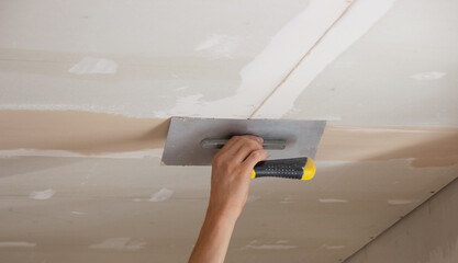 A man puts putty on a plasterboard ceiling. Putty for the joints of plasterboard sheets