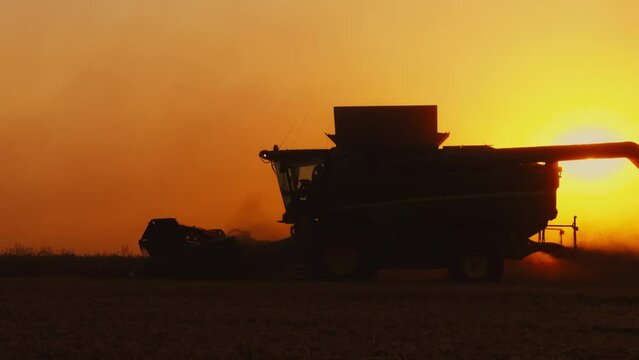 Combine harvester works in the field harvesting wheat in Clouds of dust are lit by the low sun. Combine harvester harvesting in the rays of sunset. Slow motion high quality, ProRes 422, 10 bit video