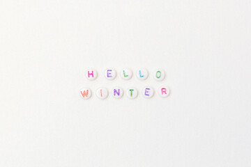 Hello winter. Quote made of white round beads with multicolored letters on a silver glittering background.