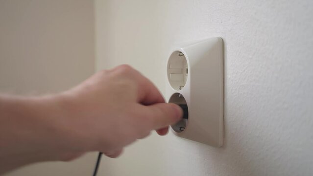 Male hand inserting black electrical plug into the socket