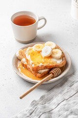 Toasts with butter, banana slices and honey on light background. Homemade breakfast sandwich and tea. Healthy vegan food concept