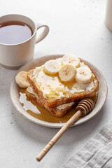 Toasts with butter, banana slices and honey on light background. Homemade breakfast sandwich and tea close up. Simple food concept