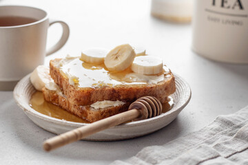 Toasts with butter, banana slices and honey on light kitchen background close up. Homemade...