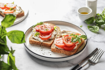 Sandwiches or toasts with tomatoes, cream cheese, olive oil and basil on a plate on white marble background. Traditional italian mediterranean food
