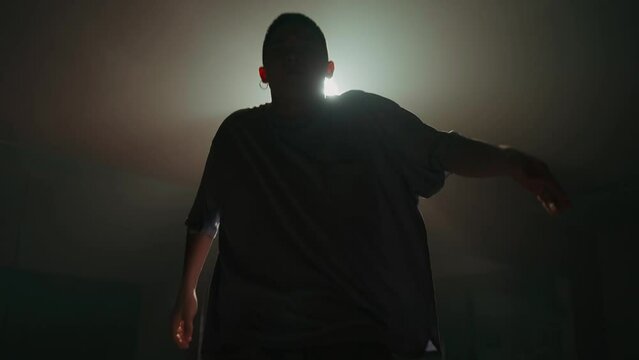 Young man dancing contemporary hip hop on red background with white light in studio wearing white shirt. Shooting of modern slow dance choreography. Motion of male dancer expressing feelings in dance