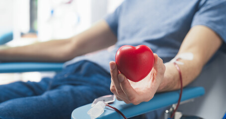 Close Up Of Hand Of Male Blood Donor With Attached Catheter. Caucasian Man Squeezing Heart-Shaped...