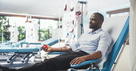 Black Man Donating Blood For People In Need In Bright Hospital. African Male Donor Squeezing...