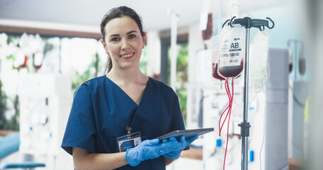 Female Nurse Holding Tablet Computer And Checking The Blood Bag In Donation Center. Professional...