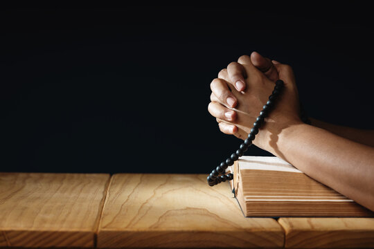 Spirituality, Religion and Hope Concept. Person Praying by Holy Bible and Bead on Desk. Symbol of Humility, Supplication, Believe and Faith for Christian People. Dark Tone.