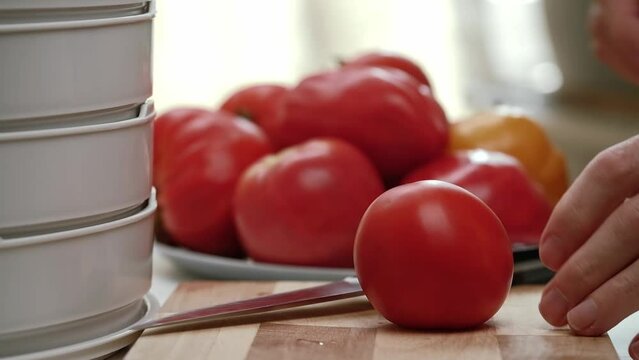 man slices ripe red tomatoes on a wooden chopping board for further drying in an electric fruit and vegetable dryer. male hands closeup. process of cooking sun dried tomatoes.