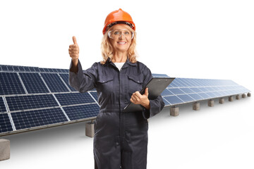 Female worker in a uniform wearing helmet and goggles and gesturing thumbs up at a solar farm