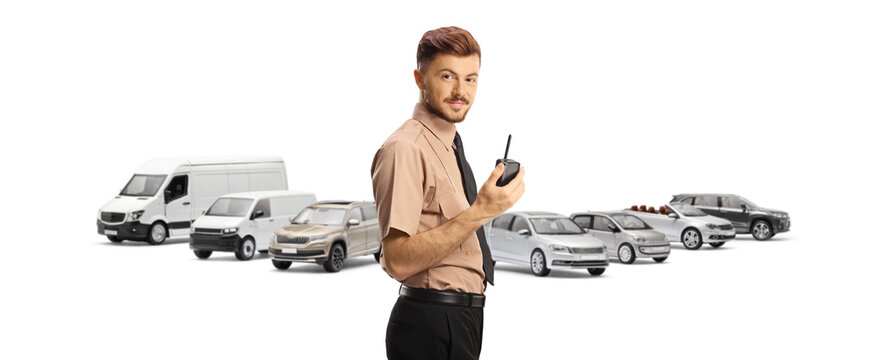 Young security guard holding a walkie talkie in front of parked vehicles