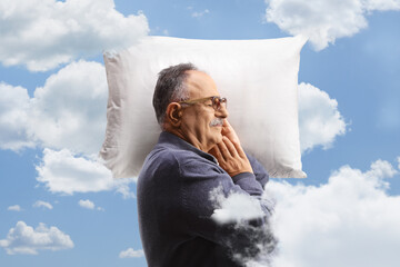 Profile shot of a mature man sleeping on a pillow between clouds