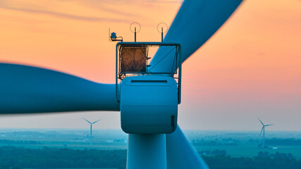Close up of motor on wind turbine with orange sunset aerial of wind farm