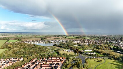Idyllic landscape of a village situated along a river with a vivid rainbow arching overhead.