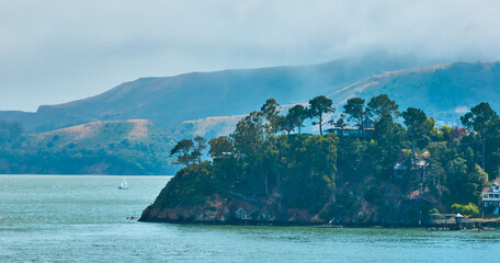 Hazy peninsula on ocean with fancy house on cliff and docks below and mountain behind aerial