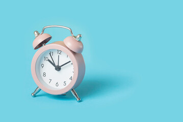 Close up one small pink metal twin bell retro alarm clock over light blue background with copy space, low angle front view