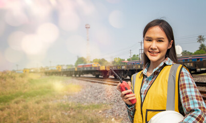 Portrait professional Asian female worker engineer working in outdoor field at diesel locomotive train station, holding walkie talkie and helmet, smiling at camera in elegant pose.