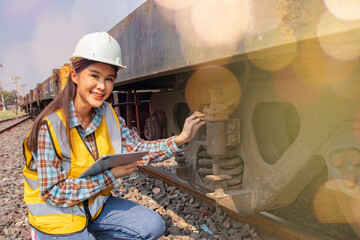 Female railway technician engineer wearing hardhat and vest does field work inspecting bogies underbody device that supports the weight train carriages responsibly controls sway of the train wheels. - obrazy, fototapety, plakaty