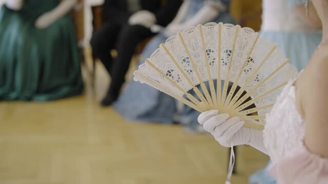 Dances of the 19th century. Lady with a fan at a ball, costumes from the 18th century. Victorian woman in a ball gown holding a fan. Girl with a fan in her hands, close-up.