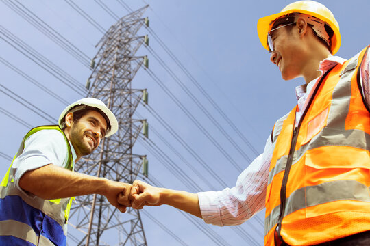 Caucasian male architect and worker asian engineer electrician bumping fists working as a team colleagues believe positive approach to success planning sustainable high voltage electric power project.