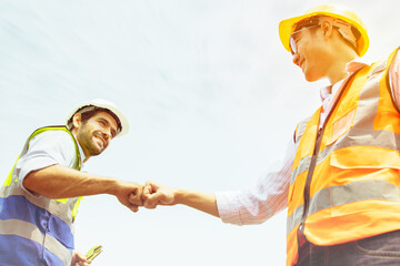 Two engineers success : Caucasian male architect worker and asian engineer  worker bumping fists...