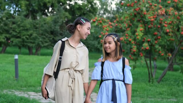 Two girls walking in the park in the summer, talking, walking after school and college, holding hands, best friends, sisters returning home after school