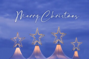 Merry christmas wishes at xmas market in pleasant advent mood. Wonderful x-mas season scene for visual or greetings card. Beautiful market tents with magic orange stars and blue sky at evening time - 665065025