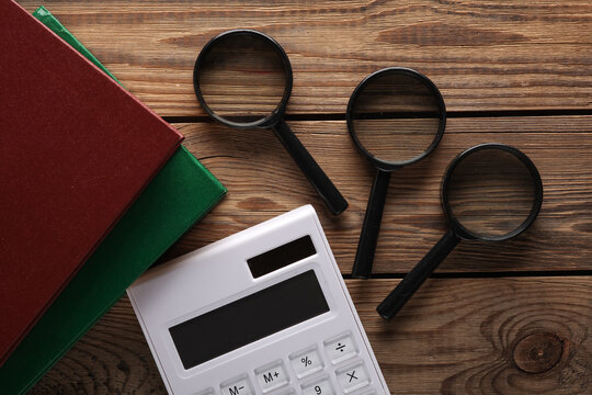 Calculator with magnifiers and books on wooden background