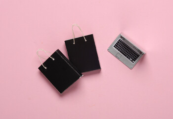 Miniature laptop with shopping bags on pink background. Online shopping