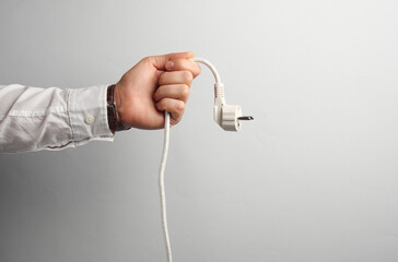 Man's hand in white shirt holds electrical plug on gray background