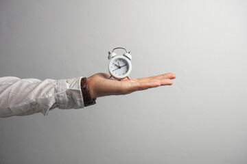 Man's hand in white shirt holds alarm clock on gray background