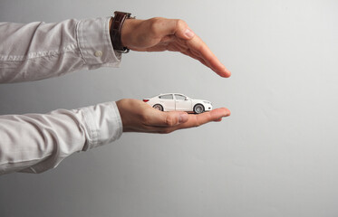 Man's hand in white shirt holds toy car on gray background. Auto insurance