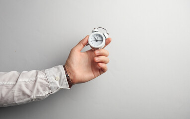 Man's hand in white shirt holds alarm clock on gray background