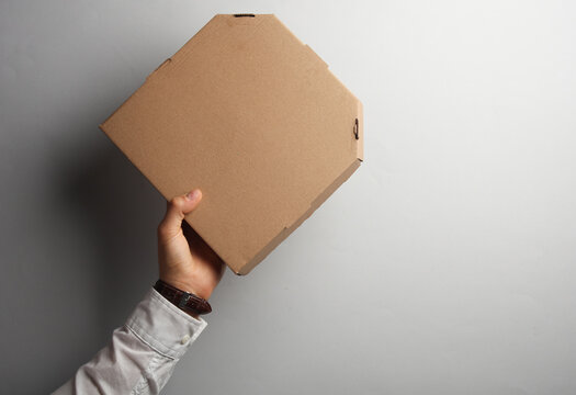 Man's hand in white shirt holds pizza box on gray background