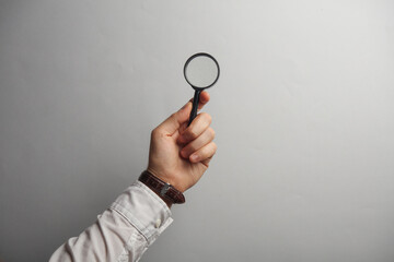 Man's hand in white shirt holds magnifying glass on gray background