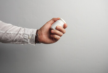 Man's hand in white shirt holds pills bottle on gray background