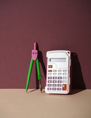 Compasses with a calculator on a beige-burgundy background. Creative layout