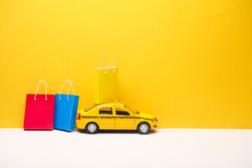 Toy taxi car with Miniature paper shopping bags on yellow gray background. Black Friday, world shopping day, holiday sale concept