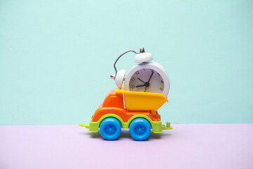 Fototapeta premium Toy dump truck with alarm clock on a pastel background