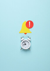 Paper cut notification bell icon and alarm clock on blue background