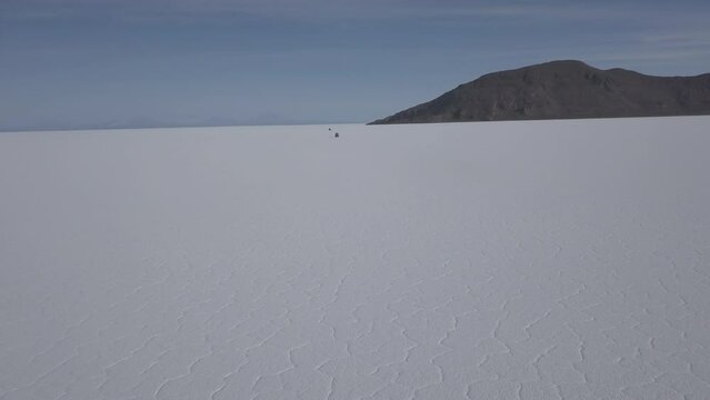 Aerial drone shot of a 4x4 offroad vehicle driving on the Salar de Uyuni salt lake around the isla pescado, fish island, on the biggest salt flat in the world in high altitude of the Andes in the Boli