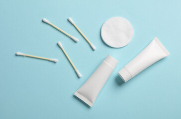 Cream tubes with cotton pads and ear buds on a blue background