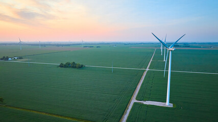Aerial row of wind turbines in green farmland fields at sunrise or sunset with orange and pink sky © Nicholas J. Klein
