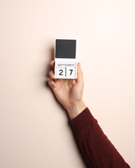 Man's hand in sweater holds block calendar with the date september 27 on a beige background