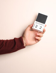 Man's hand in sweater holds block calendar with the date september 22 on a beige background