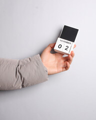 Man's hand in warm down jacket holds block calendar with date november 2 on gray background