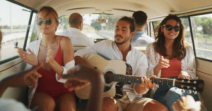 Footage Inside a Van: Slow Motion of Young Multiethnic Friends Dancing and Signing During a Road Trip. Stylish Joyful Men and Women Having Fun While Playing Guitar in Traveling Minivan. Handheld Shot