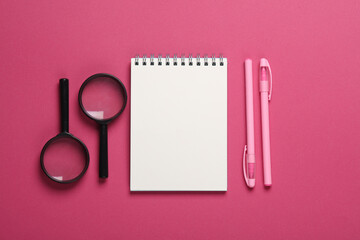 Notepad with magnifiers and pens on a pink background